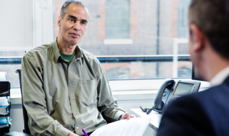 a man in an office, talking to someone in the foreground. 